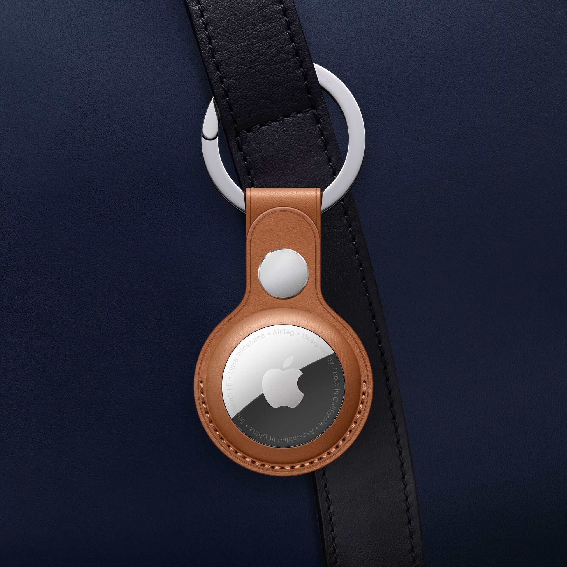 Apple AirTag i brun lædernøglering fra Apple AirTag 4-pak fastgjort til mørkeblå taskerem med sølvfarvet beslag.