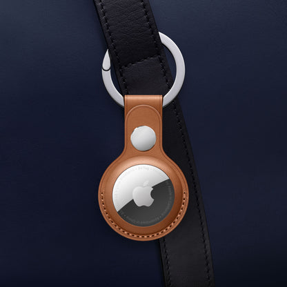 Apple AirTag i brun lædernøglering fra Apple AirTag 4-pak fastgjort til mørkeblå taskerem med sølvfarvet beslag.