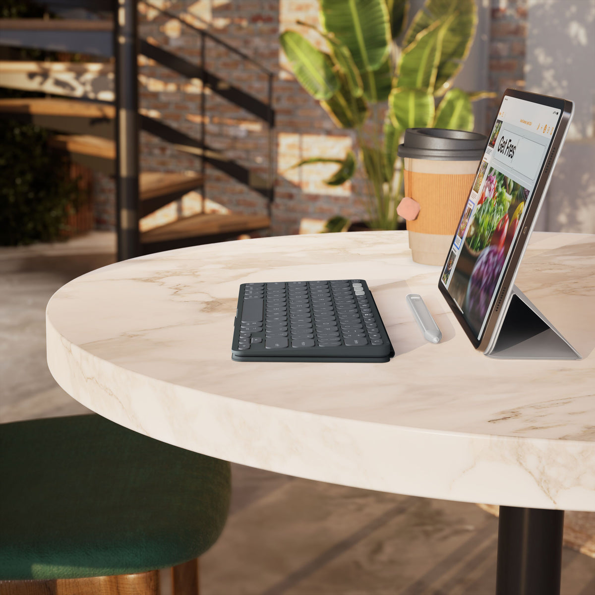 Logitech Keys-To-Go 2 bærbart Bluetooth-tastatur, sort, med stylus, kaffekop og tablet på et rundt marmorbord.