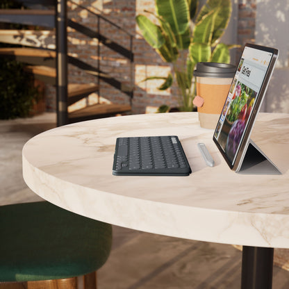 Logitech Keys-To-Go 2 bærbart Bluetooth-tastatur, sort, med stylus, kaffekop og tablet på et rundt marmorbord.