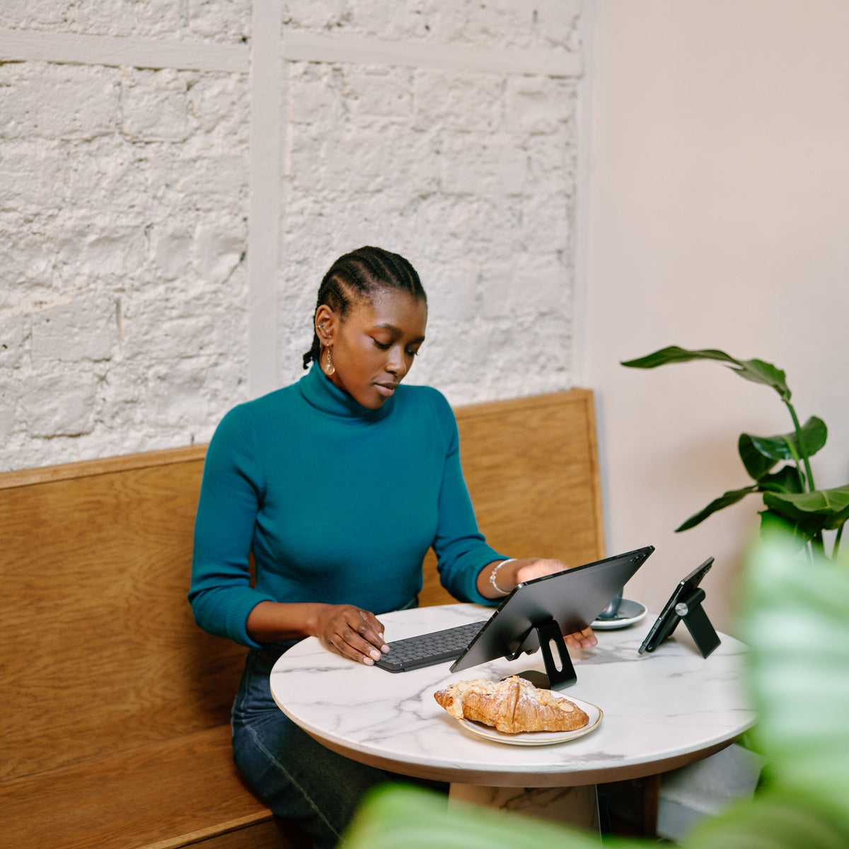 Placer Logitech Keys-To-Go 2 bærbart Bluetooth-tastatur og tablet på stativet ved cafébordet.