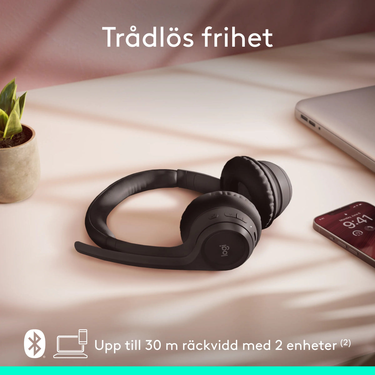 Logitech Zone 300 trådløst Bluetooth-headset i grafitfarve med mikrofonarm på skrivebordet ved siden af smartphone og bærbar computer.