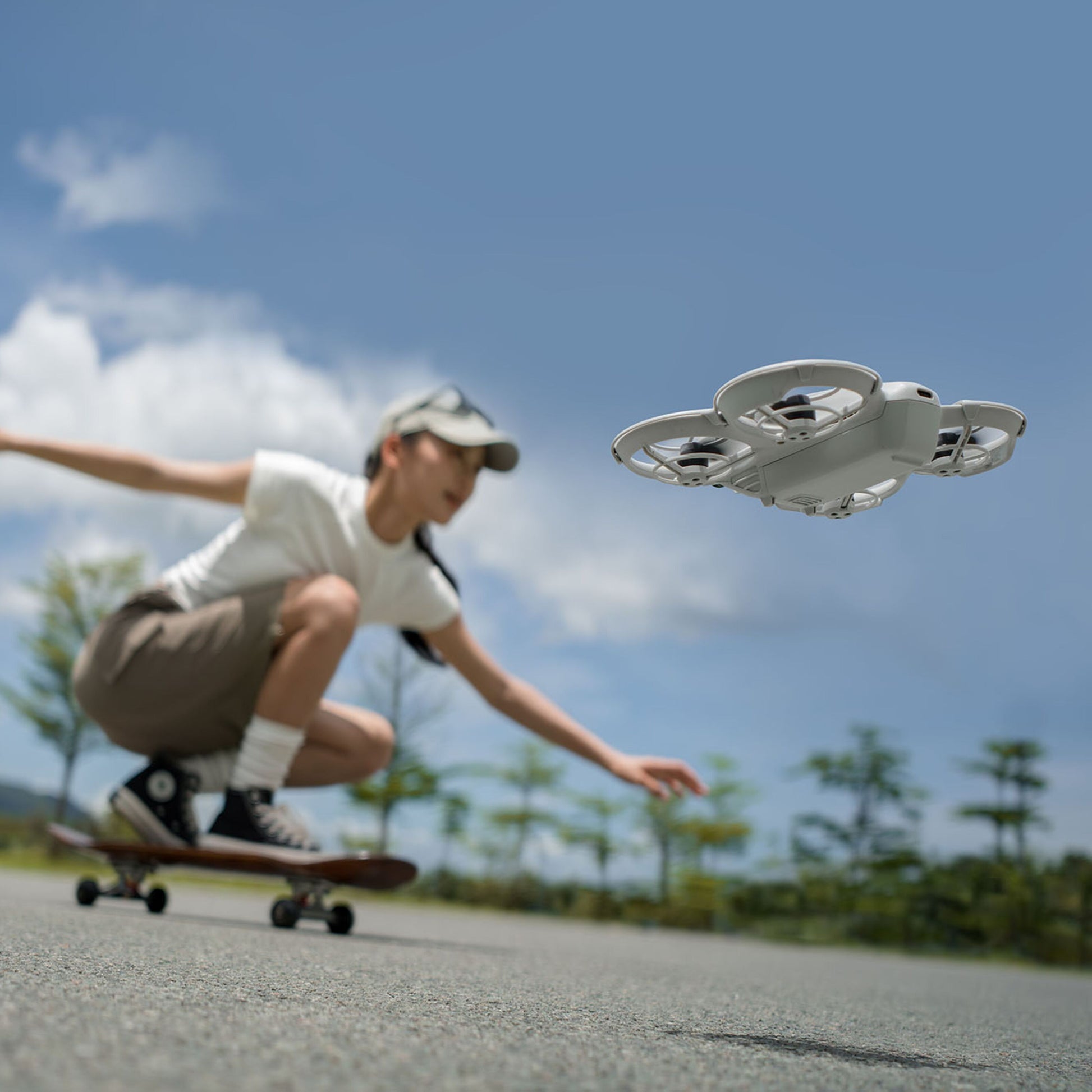 DJI Neo drone flyver i forgrunden udendørs med skateboarder, synlig model og grå himmel med skyer.