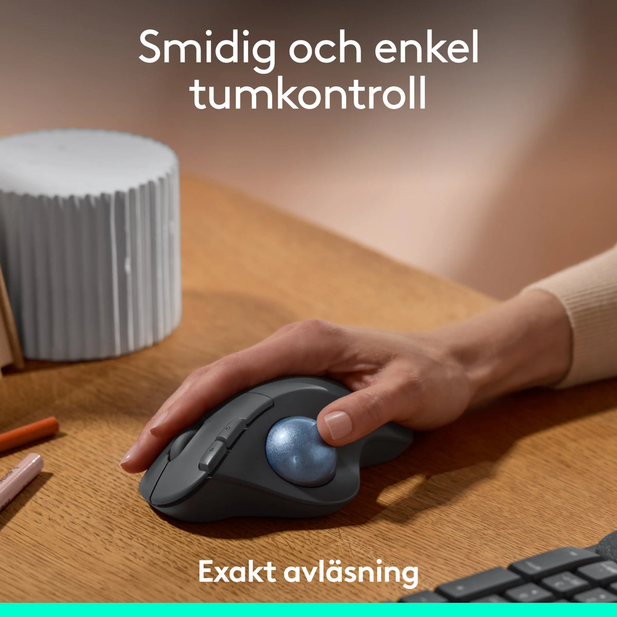 Logitech Ergo M575S trådløs trackball-mus i grafitfarve på et træbord med informationstekst om tommelfingerbetjening og præcis sporing.
