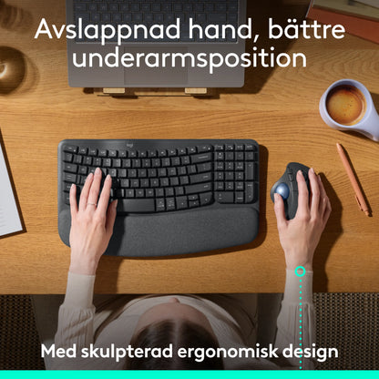 Ergonomisk tastatur og mørkegrå Logitech Ergo M575S trådløs trackball-mus på et træbord.