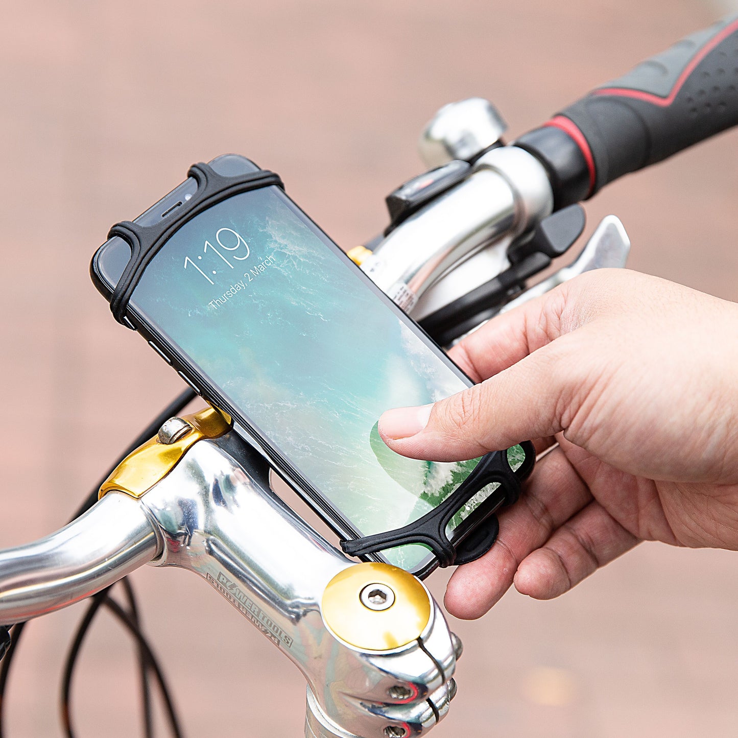 Smartphone i Linocell Mobilholder silikone monteret på cykelstyr, skærm viser 1:19, sølvstyr og greb synlige.
