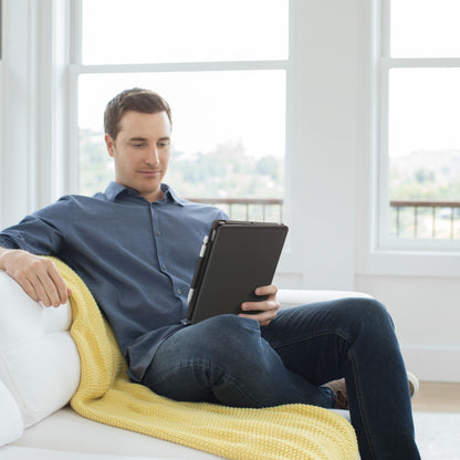 IPad 10,2 med Slim Folio Tastaturcover bruges på hvid sofa med gul plaid, mand i blå skjorte og jeans.