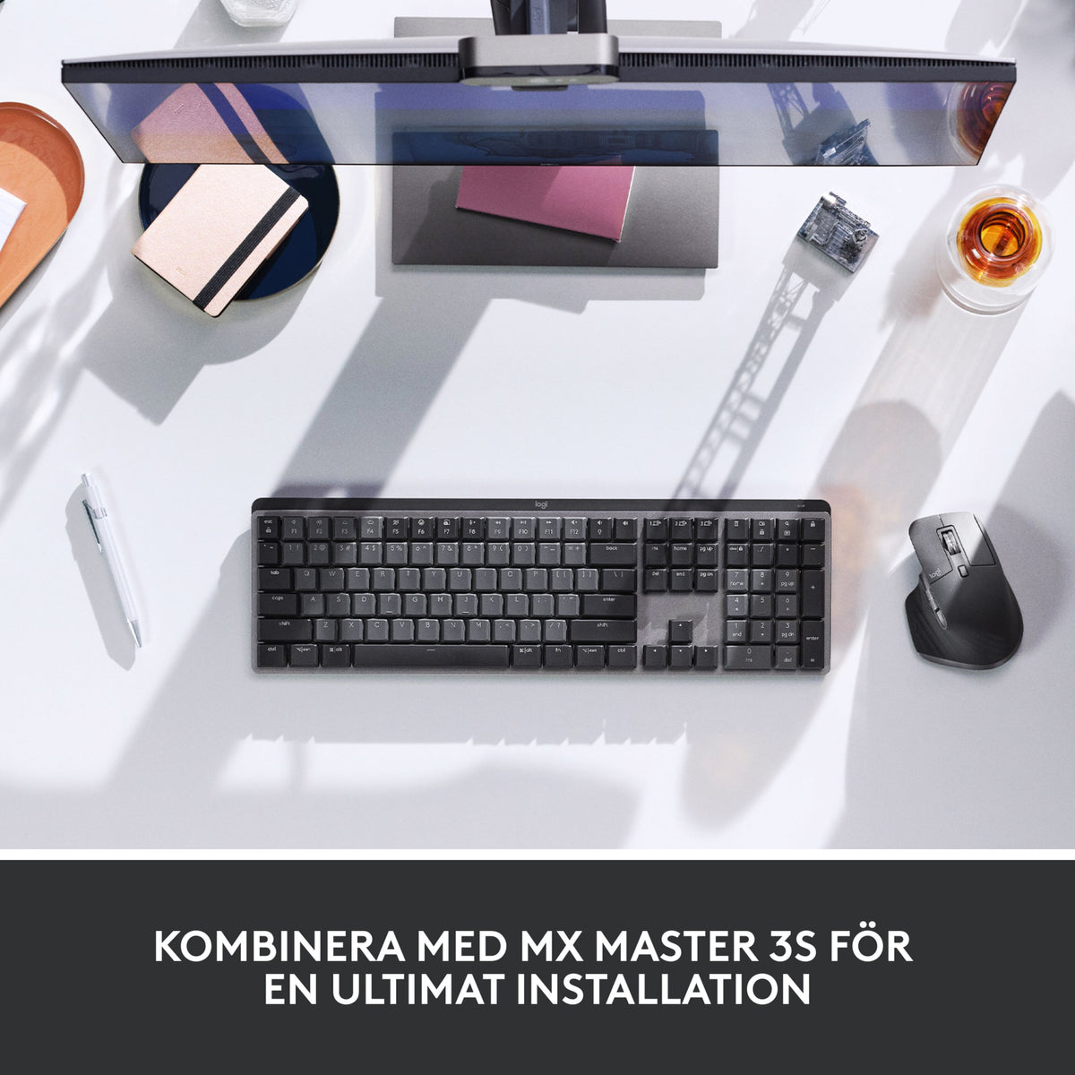 Logitech MX Mechanical trådløst mekanisk tastatur (Tactile Quiet Brown) og computermus på et skrivebord med skærm, pen og glas.