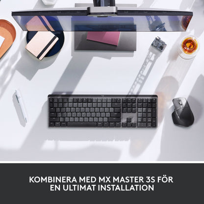 Logitech MX Mechanical trådløst mekanisk tastatur (Tactile Quiet Brown) og computermus på et skrivebord med skærm, pen og glas.