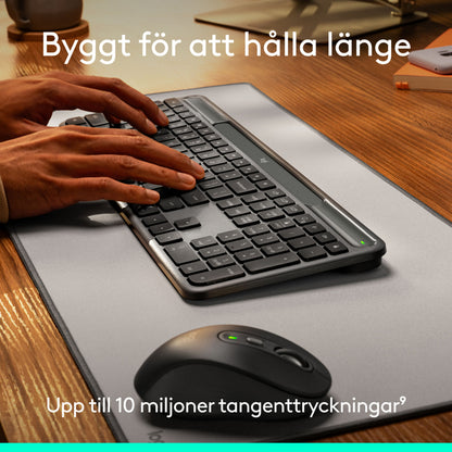 Hænder, der skriver på et Logitech Signature Slim Solar+ trådløst tastatur med solopladning og en mus på en bordunderlag.