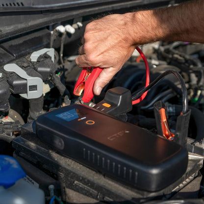 Ctek RB 3000 Startbooster 59,2 Wh, røde startkabler forbindes til bærbar bilbatteri jumpstarter under motorhjelm.
