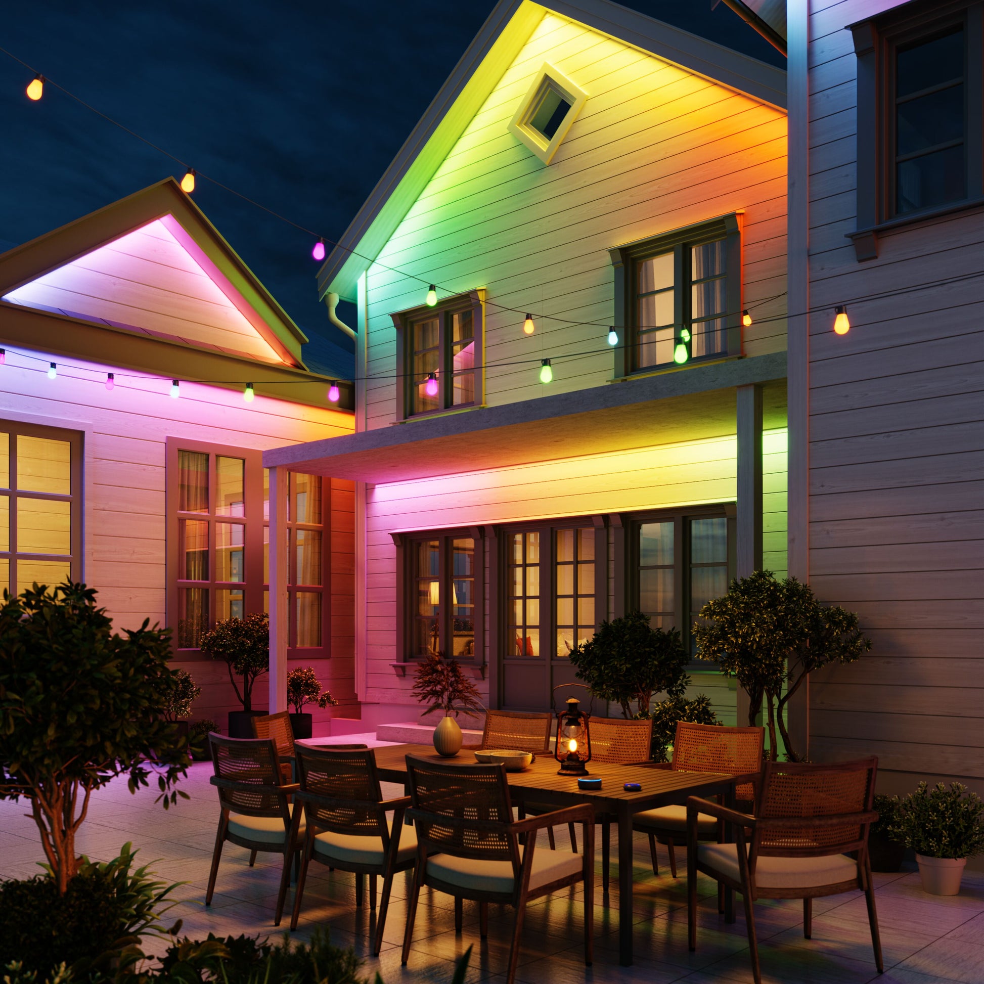 Govee Udendørs Strip Light Pro RGBICWW 10 m lyser husfacade op i regnbuefarver, terrassebord og planter synlige.