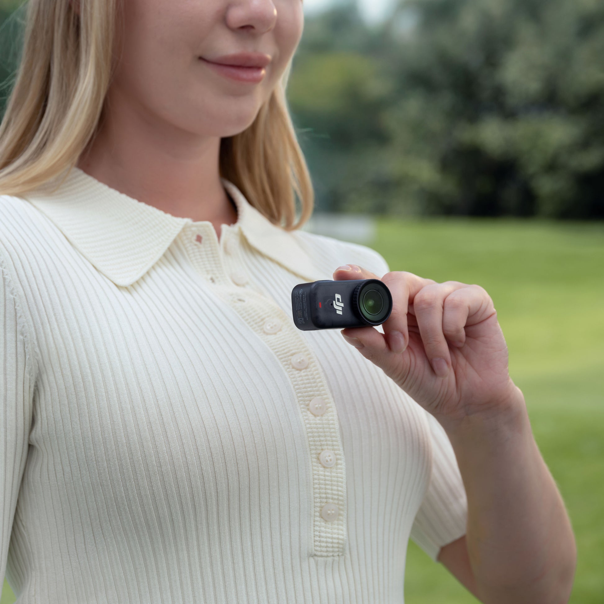 DJI Osmo Nano actionkamera 128 GB med grøn linse holdes i hånden, cremefarvet ribbet skjorte synlig.