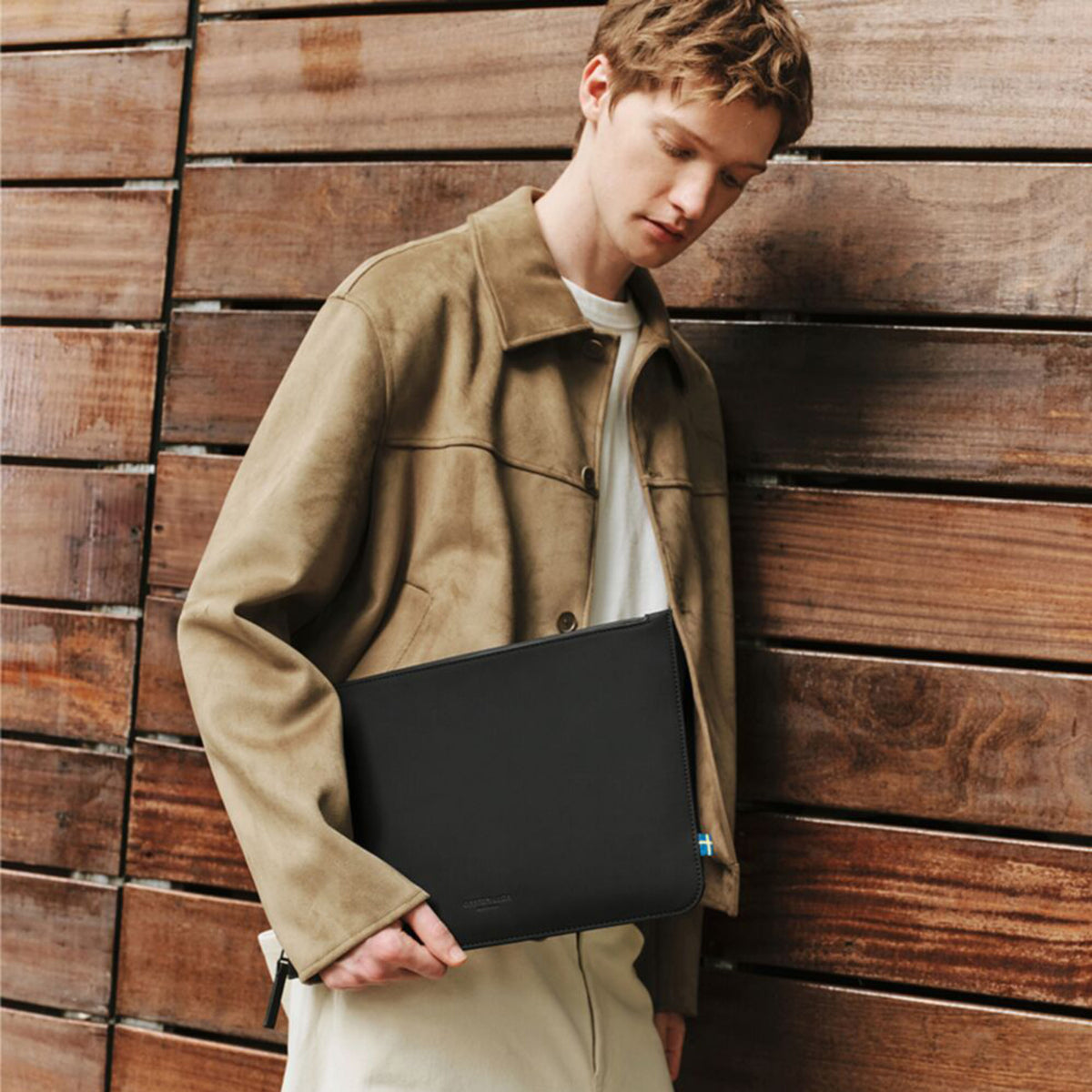 Gaston Luga Däsh laptop-taske (13–14″) i sort, som en person i en beige jakke og en hvid skjorte holder under armen.