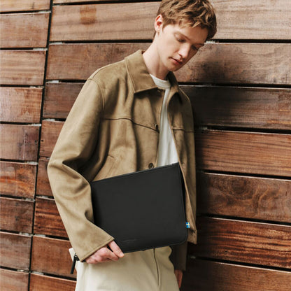 Gaston Luga Däsh laptop-taske (13–14″) i sort, som en person i en beige jakke og en hvid skjorte holder under armen.