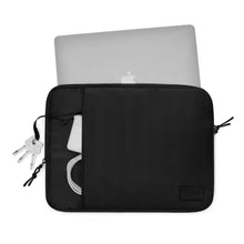 Apple MacBook i Gaston Luga Däsh polstret taske 13/14″, sort, synligt Apple-logo, opladerkabel, strømadapter og nøgler i forlommen.