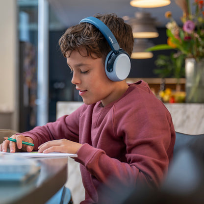 Dreng med Philips 5000-serien trådløse blå over-ear børnehøretelefoner, bærer sweatshirt, ved bord, skrivevinkel.