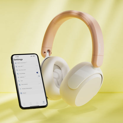 Philips trådløse over-ear hovedtelefoner til børn med støjreduktion i beige ved siden af smartphone med indstillingsmenu.