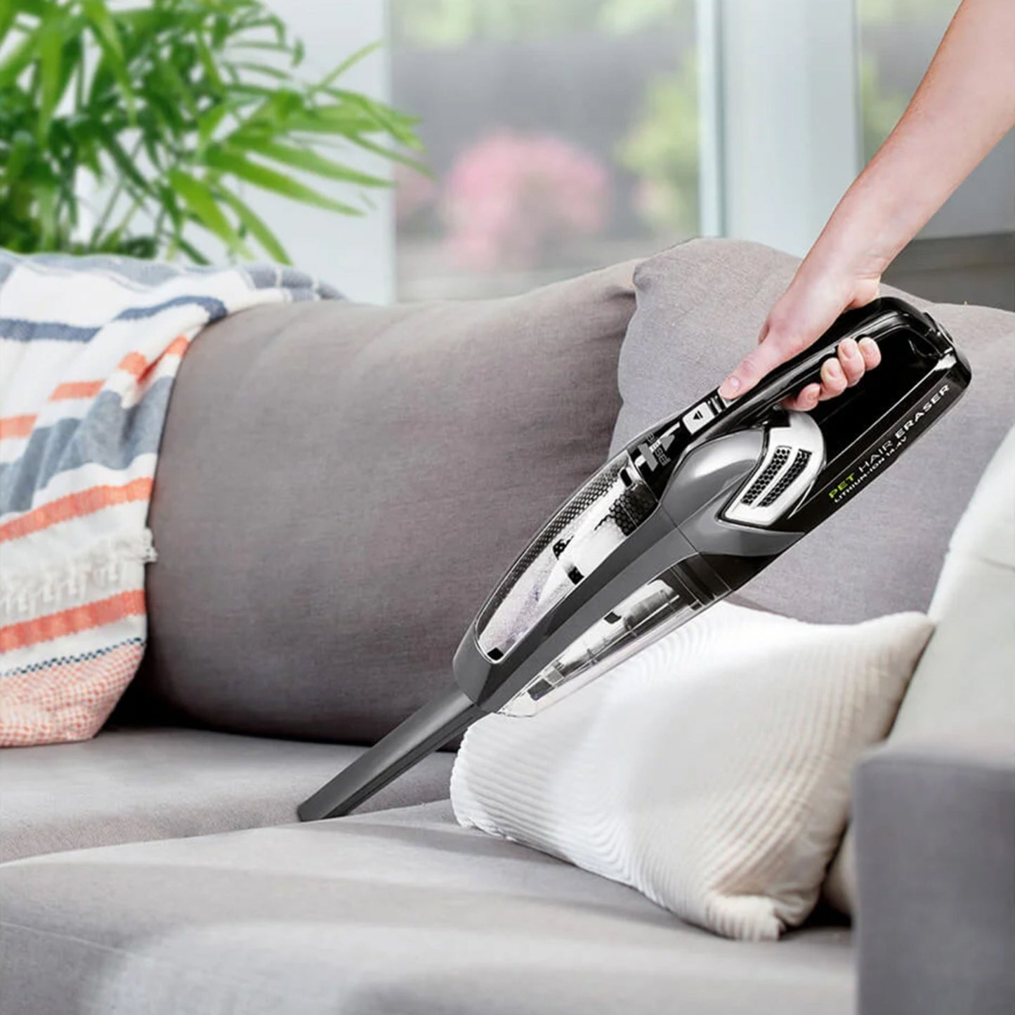 Bissel Pet Hair Eraser håndstøvsuger 14,4 V fjerner krummer og dyrehår fra grå sofa med farverigt tæppe.