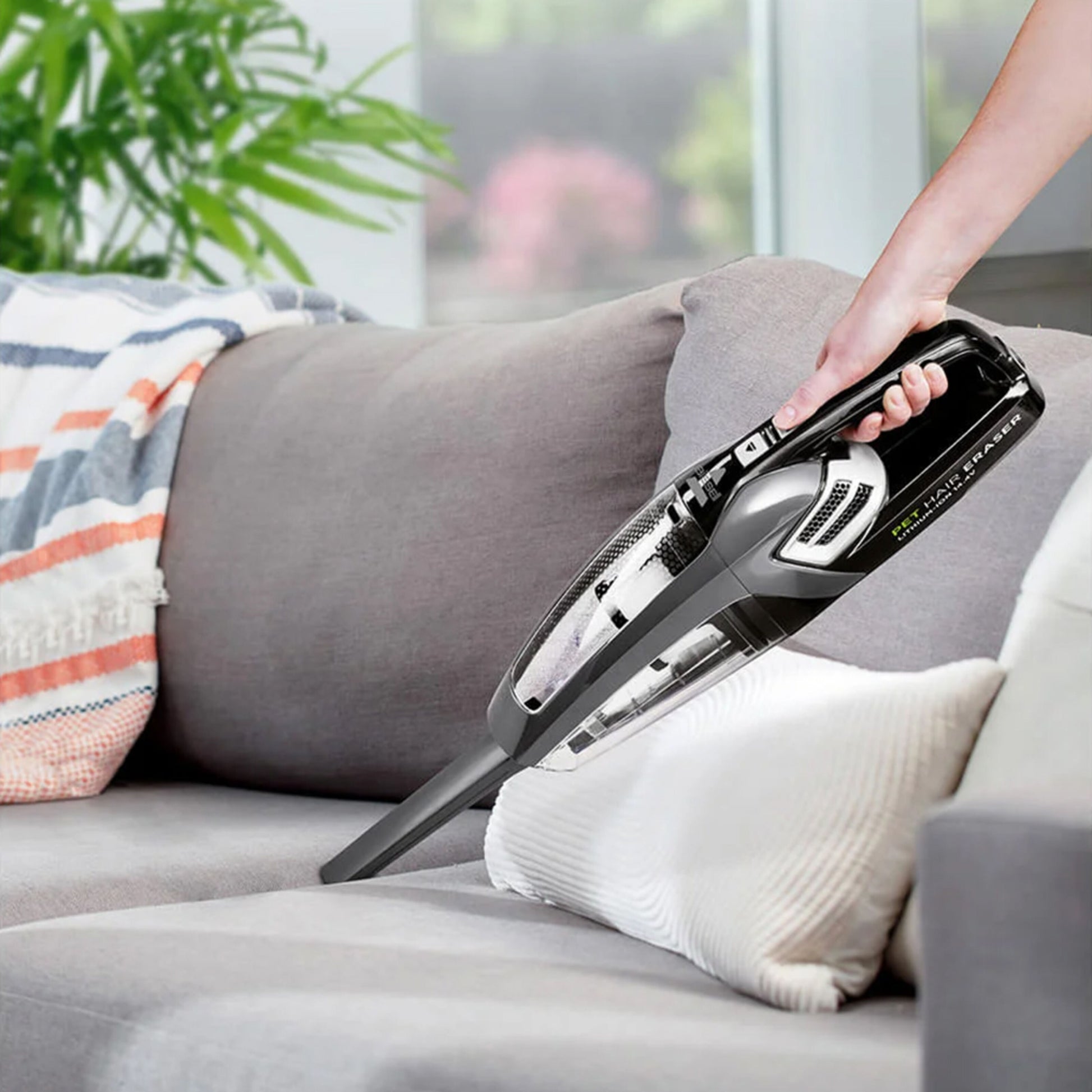 Bissel Pet Hair Eraser håndstøvsuger 14,4 V fjerner krummer og dyrehår fra grå sofa med farverigt tæppe.