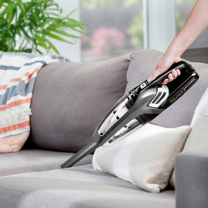 Bissel Pet Hair Eraser håndstøvsuger 14,4 V fjerner krummer og dyrehår fra grå sofa med farverigt tæppe.