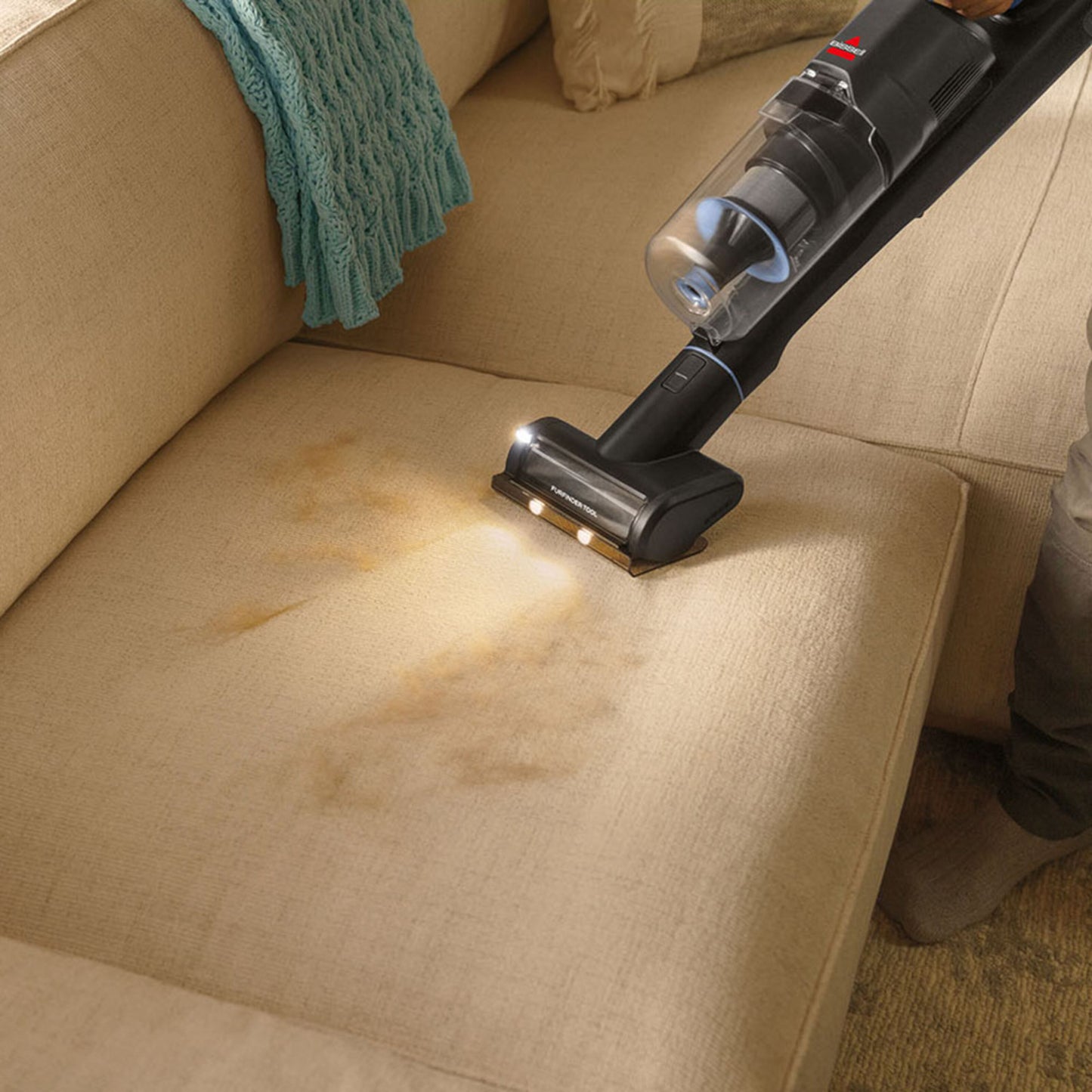 Bissel PowerClean FurFinder Select skaftstøvsuger fjerner dyrehår fra lys brun stofsofa med pletter, blå plaid på armlæn.
