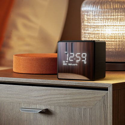 Philips R4600 DAB+ vækkeur sølv med USB-C-opladning, display viser 12:59 på trænatbord ved orange pude og glaslampe.