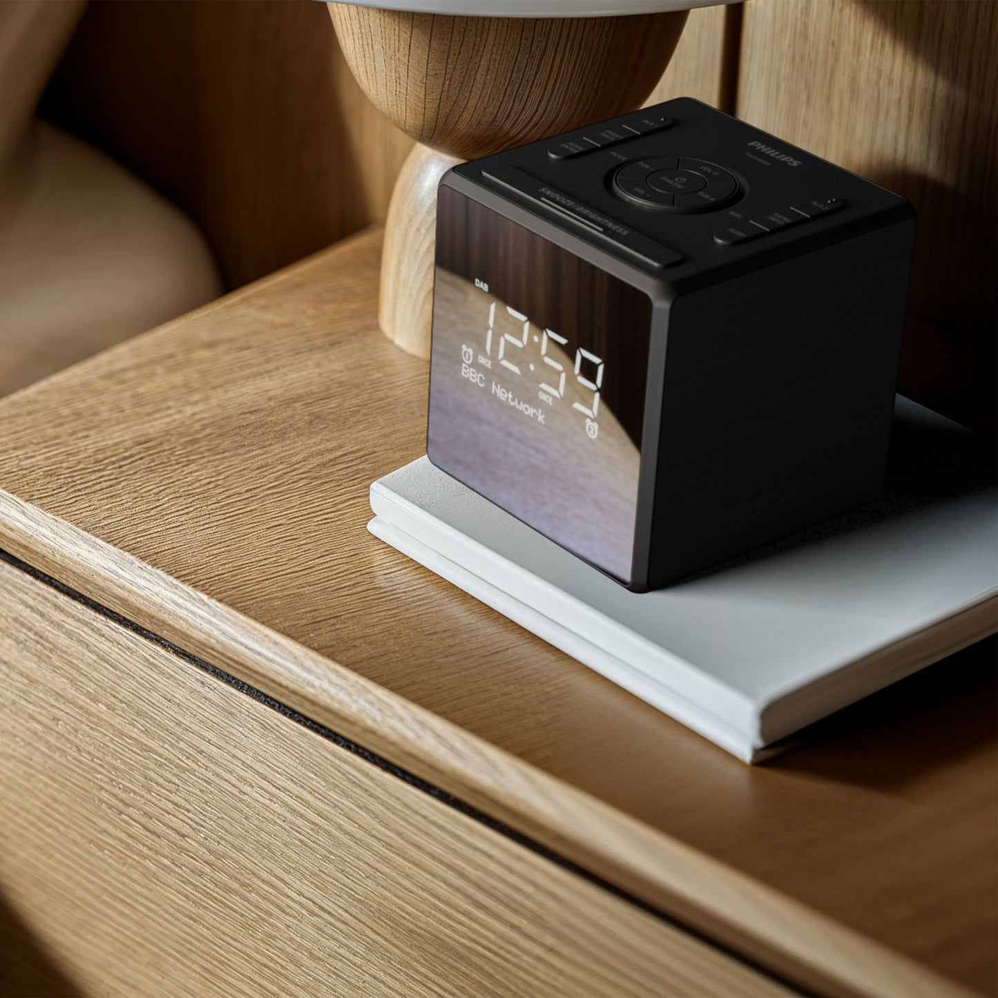 Philips R4600 DAB+ vækkeur, sølv, USB-C opladning, display viser 12:59, placeret på bog på trænatbord.