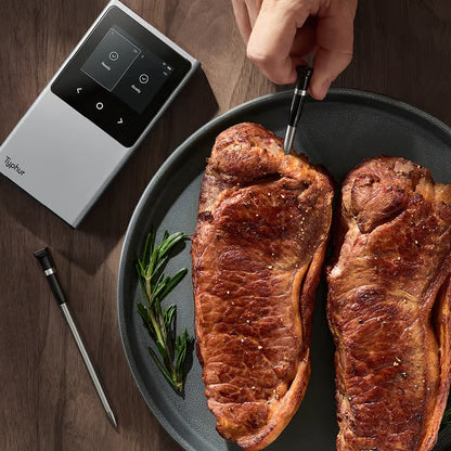 Typhur Sync Dual trådløst grill- og stegetermometer; sonden sættes ind i den stegte bøf på tallerkenen ved siden af den digitale enhed.