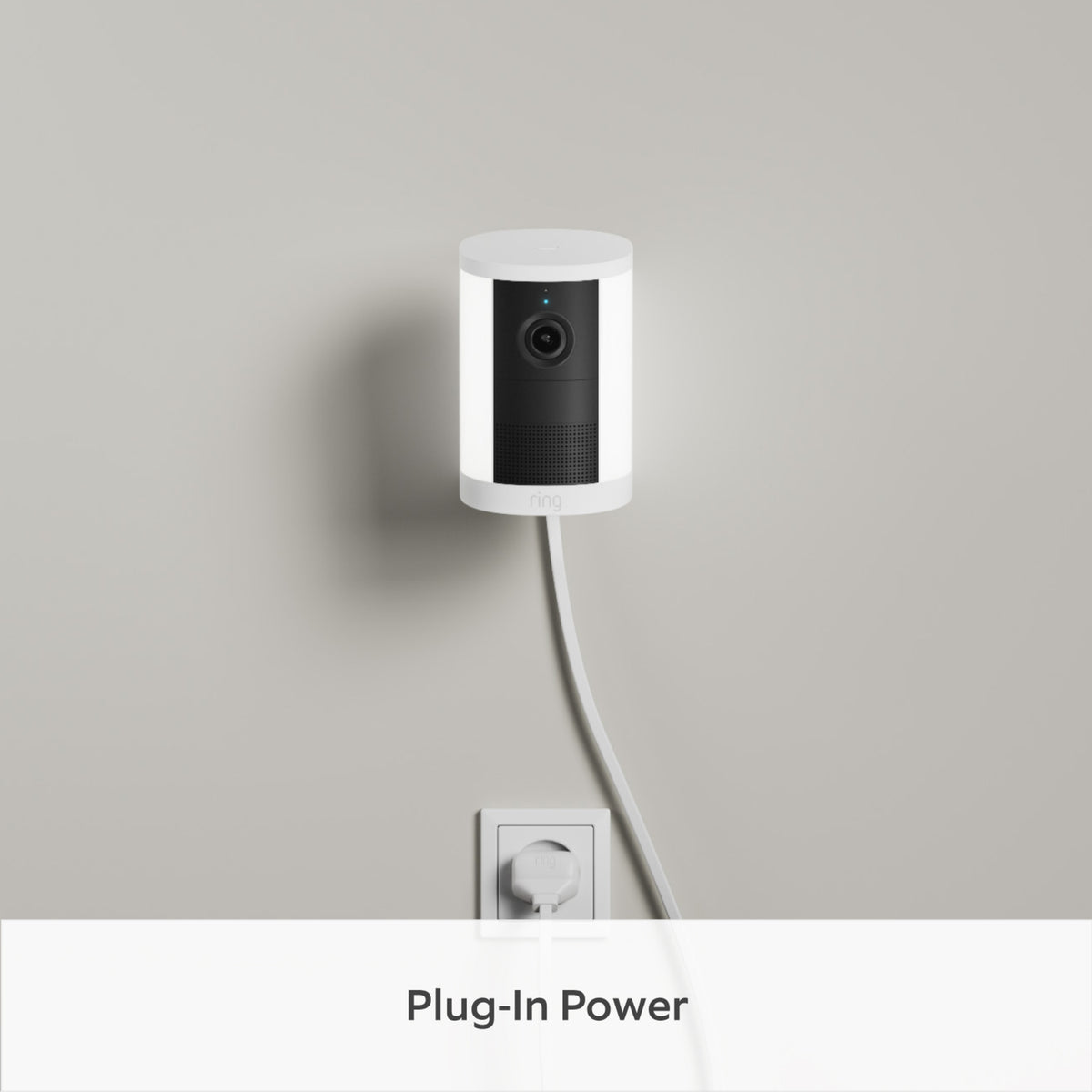 Ring Spotlight Cam Plug-in Retinal 2K, monteret på en lysegrå væg, tilsluttet det nederste stik med et hvidt ledning.