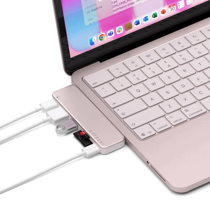 Satechi USB-C Snap Hub Neo Rouge er tilsluttet en lyserød MacBook Neo med flere kabler og et SD-kort; apps vises på skærmen.