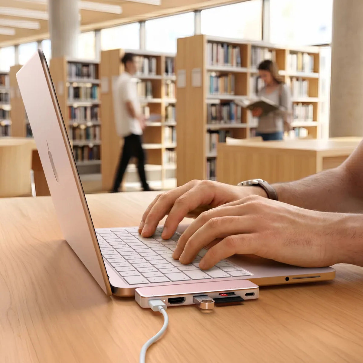 En MacBook Neo med en tilsluttet Satechi USB-C Snap Hub Neo Rouge ses på et træbord i biblioteksområdet.