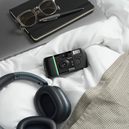 Fujifilm QuickSnap sort-hvidt engangskamera til 27 billeder, trådløse hovedtelefoner, gråt strikket tæppe, sort notesbog.
