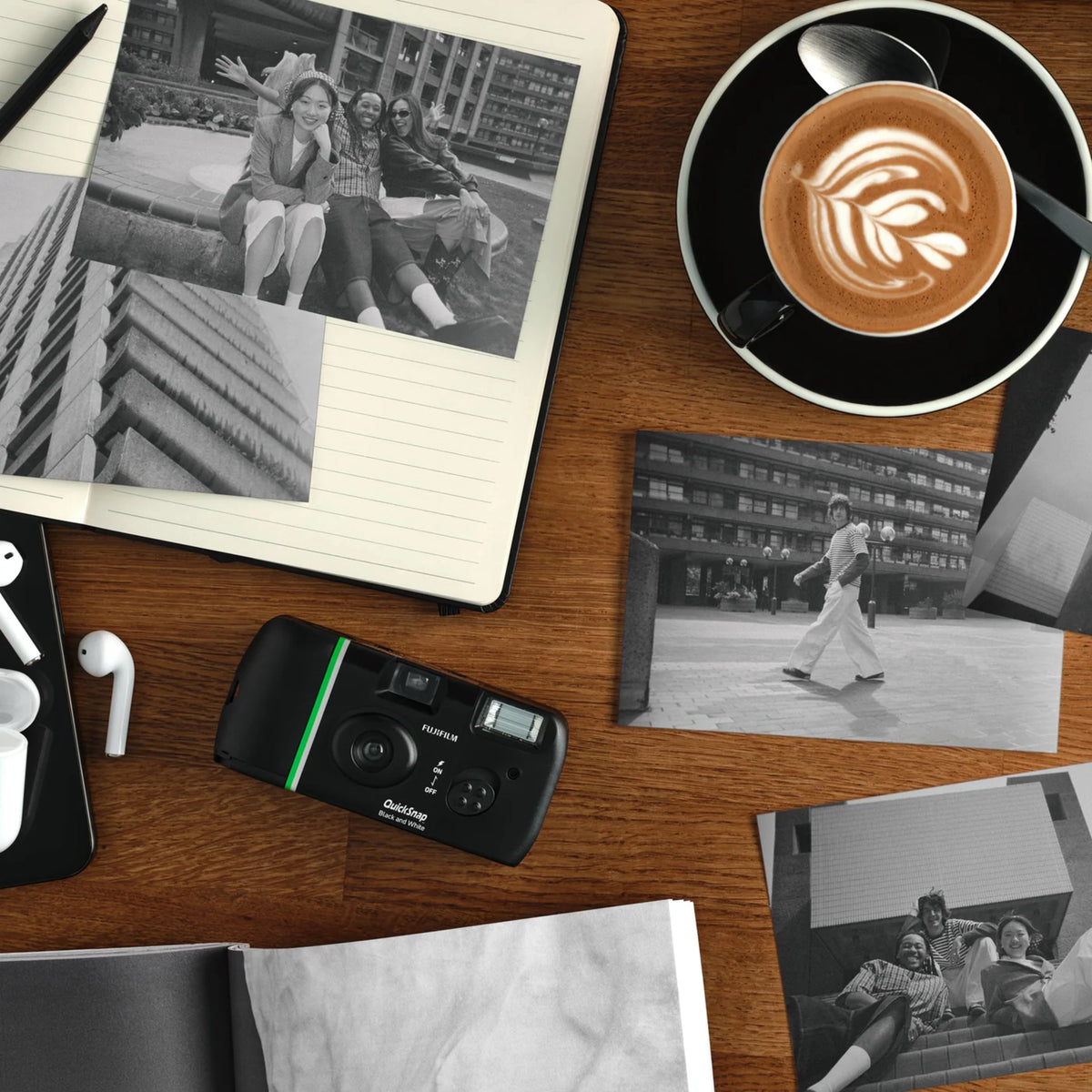 Fujifilm QuickSnap sort-hvidt engangskamera til 27 billeder ses sammen med en kaffekop, en notesbog, fotos og hovedtelefoner.
