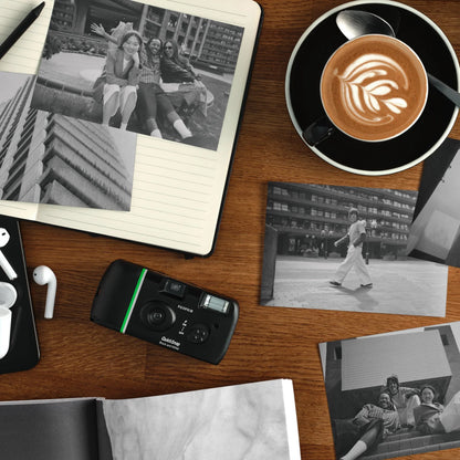 Fujifilm QuickSnap sort-hvidt engangskamera til 27 billeder ses sammen med en kaffekop, en notesbog, fotos og hovedtelefoner.