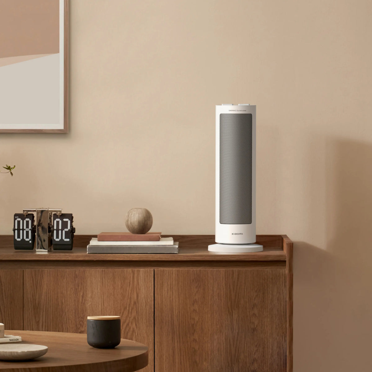 Xiaomi-varmeblæser (EU-model) med PTC-varmeelement, 2000 W, hvid, stående på et træbord ved siden af et digitalt ur, en bog og et rundt dekorativt element.