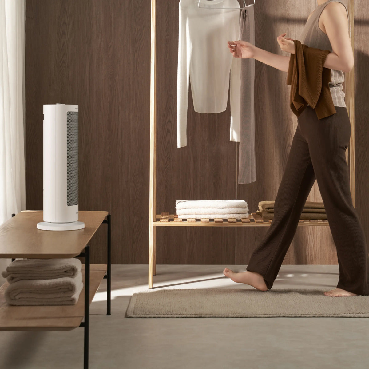 XIAOMI varmeblæser EU PTC-varmeblåser 2000 W på et bord i et lyst rum med trævæg, en person tæt ved et tøjstativ.
