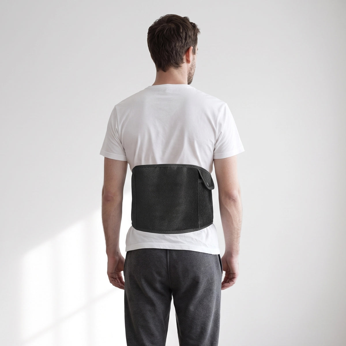 Et elektrisk varmebælte til mave og ryg med USB-C-stik, placeret omkring lænden uden på en hvid T-shirt.