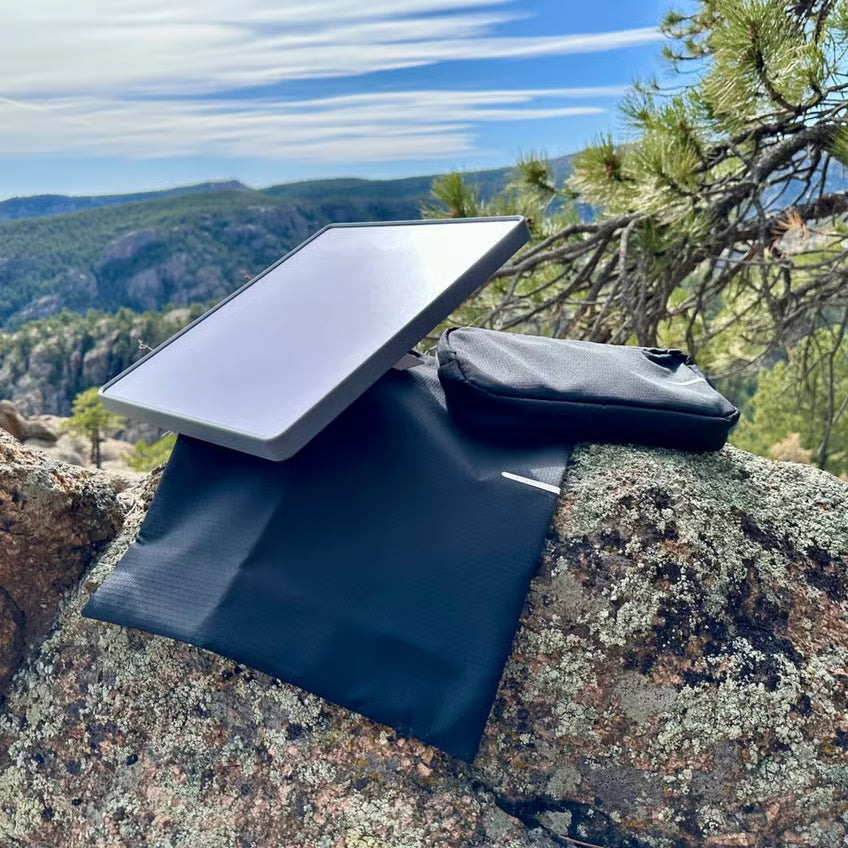 Starlink Mini-antenne med Starlink Mini Travel Kit-rejsetaske, sort taske og tilbehørspose på klippefyldt undergrund.