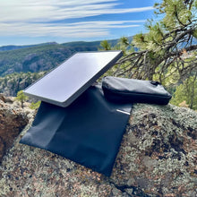 Starlink Mini-antenne med Starlink Mini Travel Kit-rejsetaske, sort taske og tilbehørspose på klippefyldt undergrund.