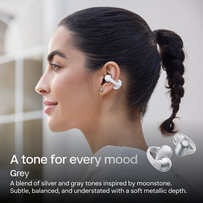Shokz OpenDots 2 åbne øretelefoner med klips, grå med DirectPitch-teknologi, båret af en kvinde; der vises to billeder af øretelefonerne.