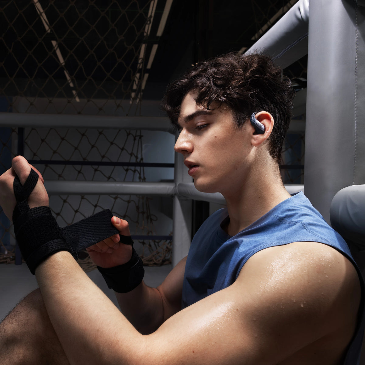SHOKZ OpenFit Air 2 åbne øretelefoner i sort bæres af en ung mand iført en ærmeløs trøje, håndbind og sved.