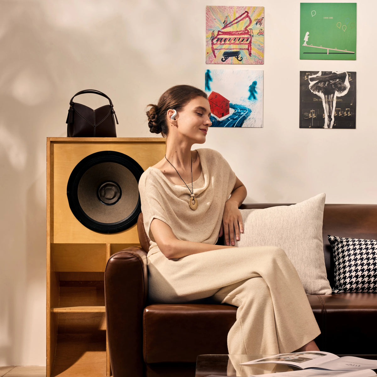 Shokz OpenFit Air 2-høretelefoner med åbne ørepropper i hvidt, båret af en kvinde, set fra siden på en brun lædersofa.