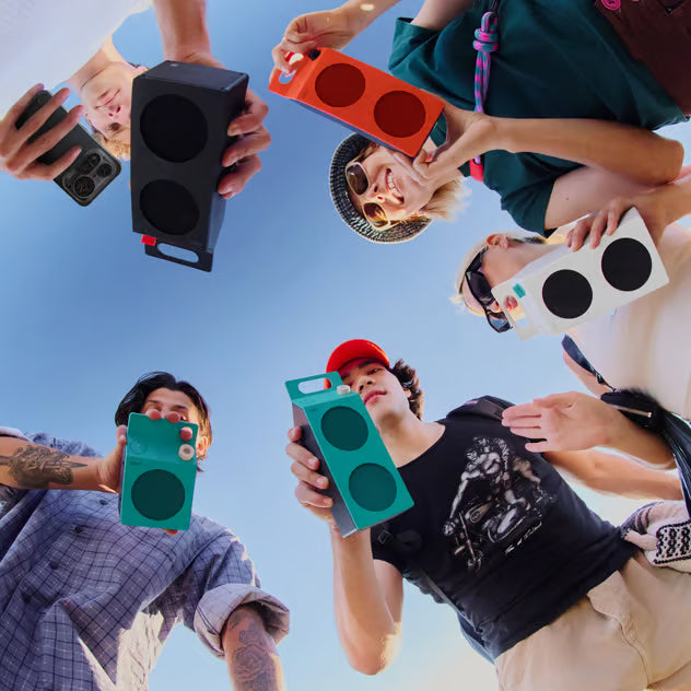 CMF by Nothing Speaker – bærbar Bluetooth-højttaler i orange, holdt af en gruppe mennesker foran en blå himmel.