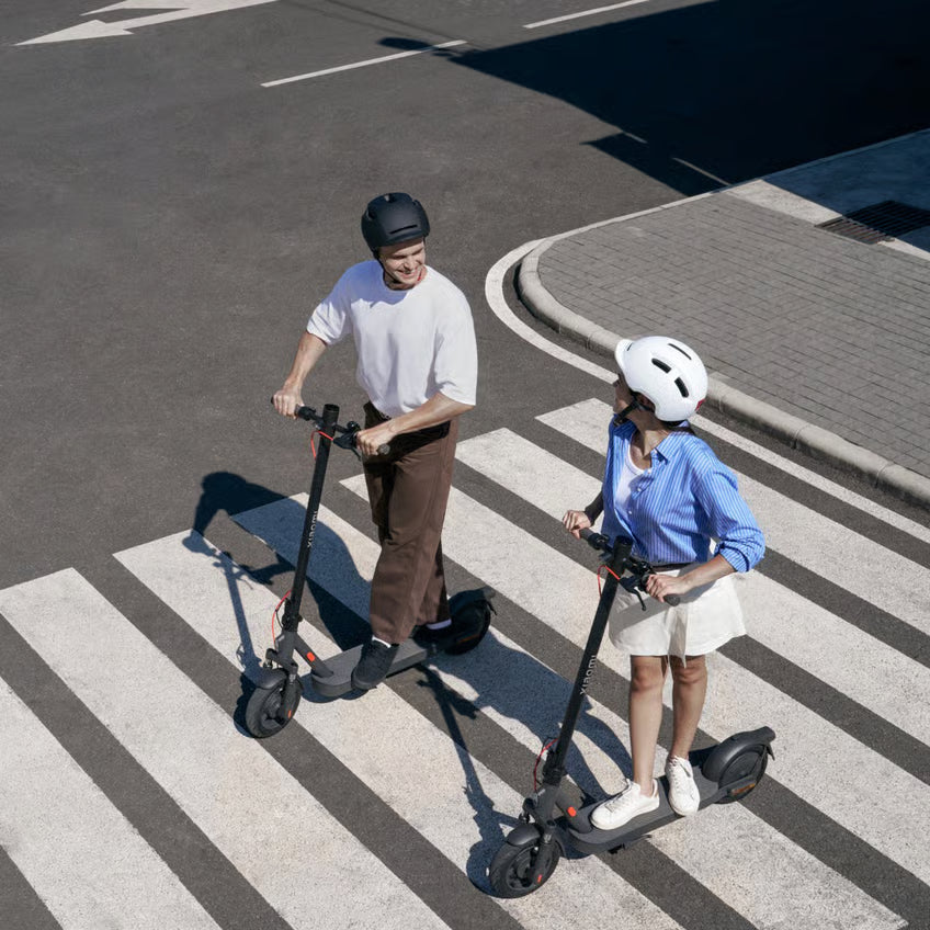 To personer på et Xiaomi Electric Scooter Elite NE-el-løbehjul med hjelm på et fodgængerovergang, 20 km/t.
