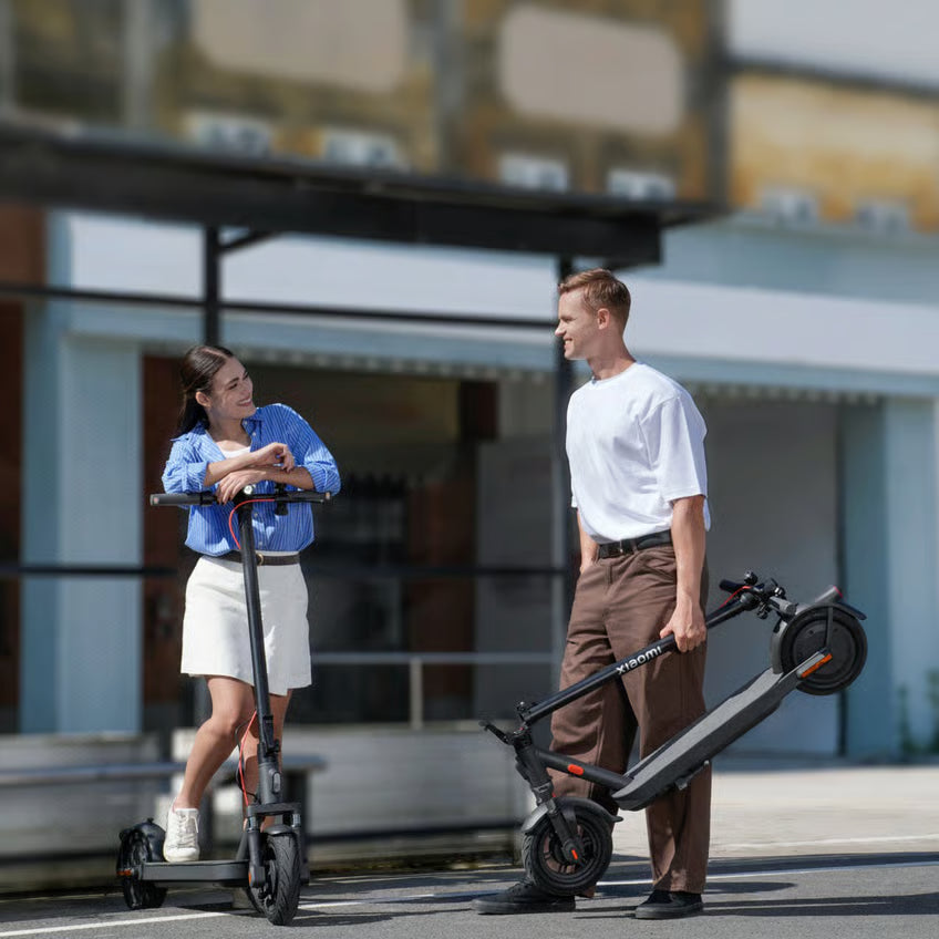En kvinde med en Xiaomi Electric Scooter Elite NE og en mand med et sammenklappet el-løbehjul udendørs.