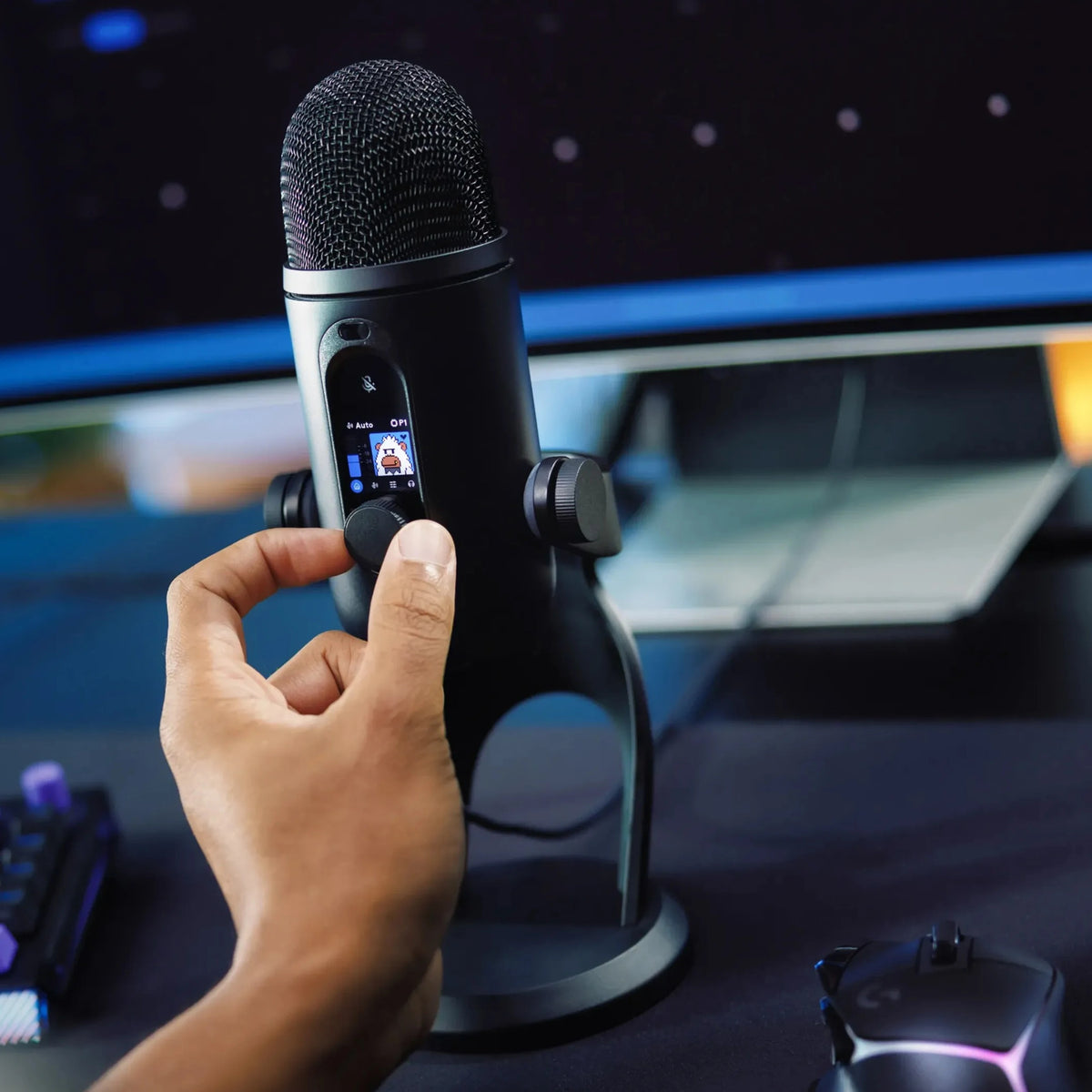 Hånden justerer drejeknappen på den sorte Logitech G Yeti 2 USB-mikrofon med AI-støjreduktion og digitalt display med ikon.