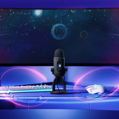 Logitech G Yeti 2 USB-mikrofon med AI-støjreduktion, skærm og stativ på skrivebordet sammen med tastatur og mus.