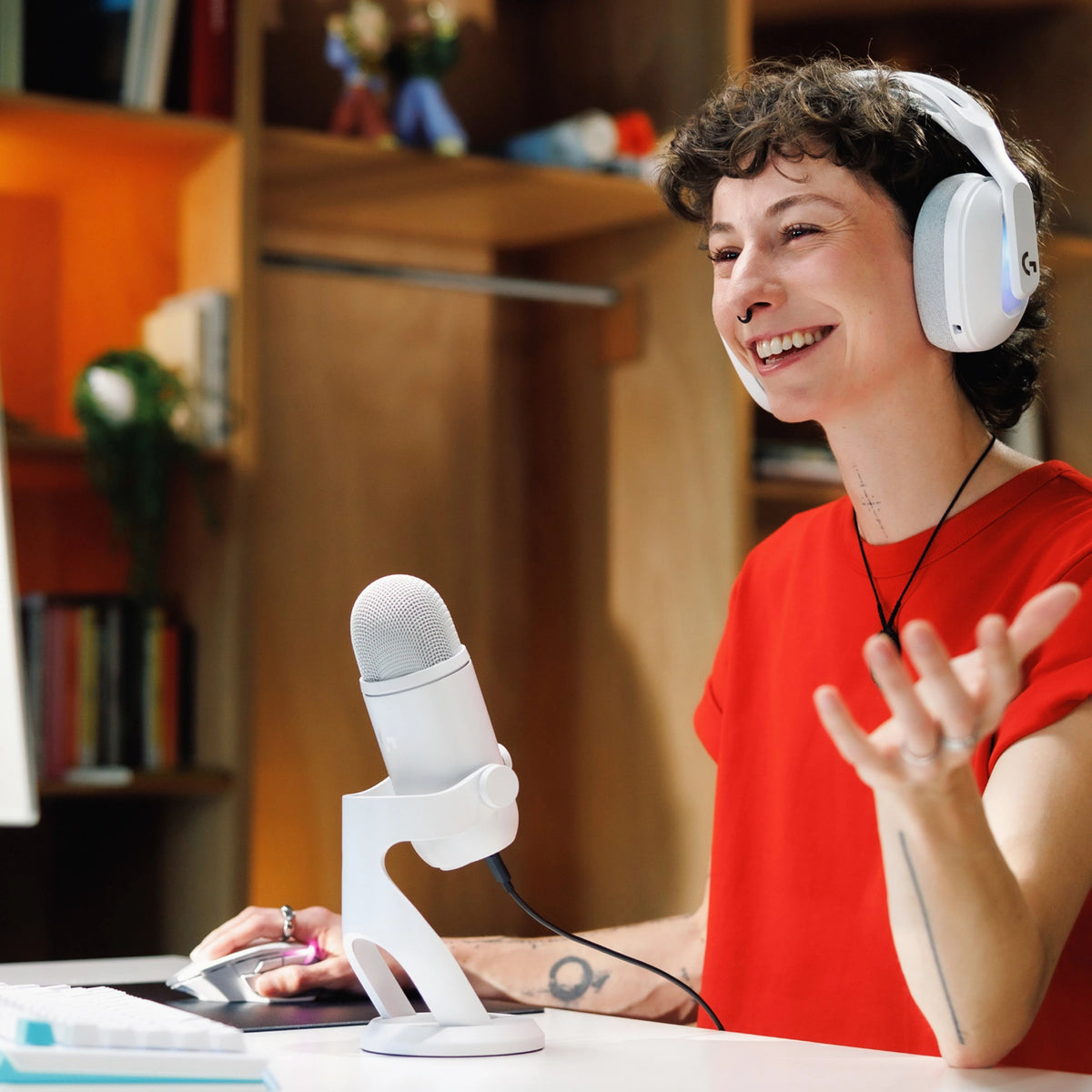 En person med hvide over-ear-hovedtelefoner taler i en hvid Logitech G Yeti 2 USB-mikrofon med AI-støjreduktion.