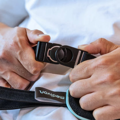 Hænder, der spænder den sorte plastspænde på en sort Medivon Motion X trådløs Shiatsu-nakkemassager.